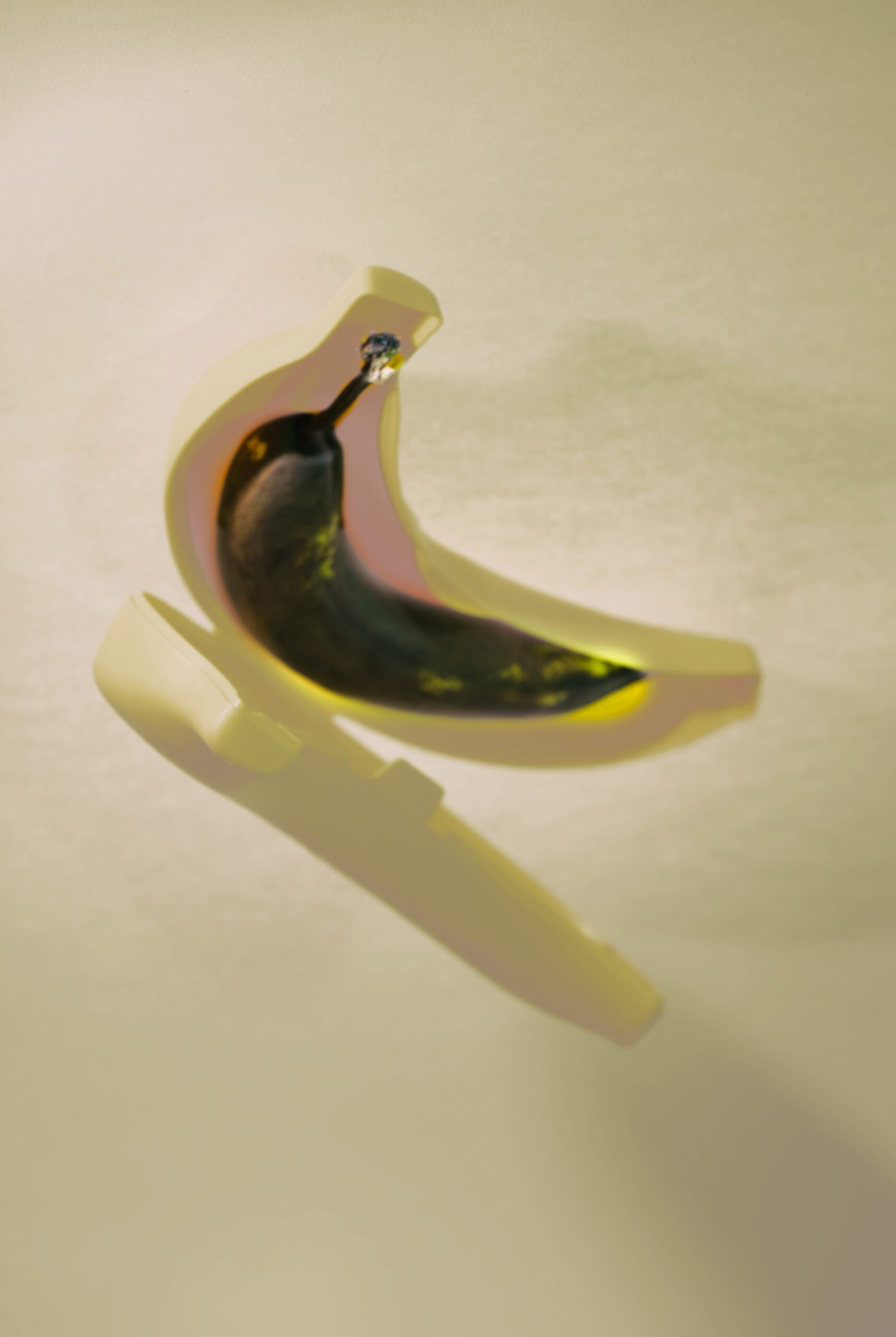 faule Banane in makelloser Plastikbanane vor neutral gelbem Hintergrund, angeblitzt, wodurch leichte Schatten entstehen