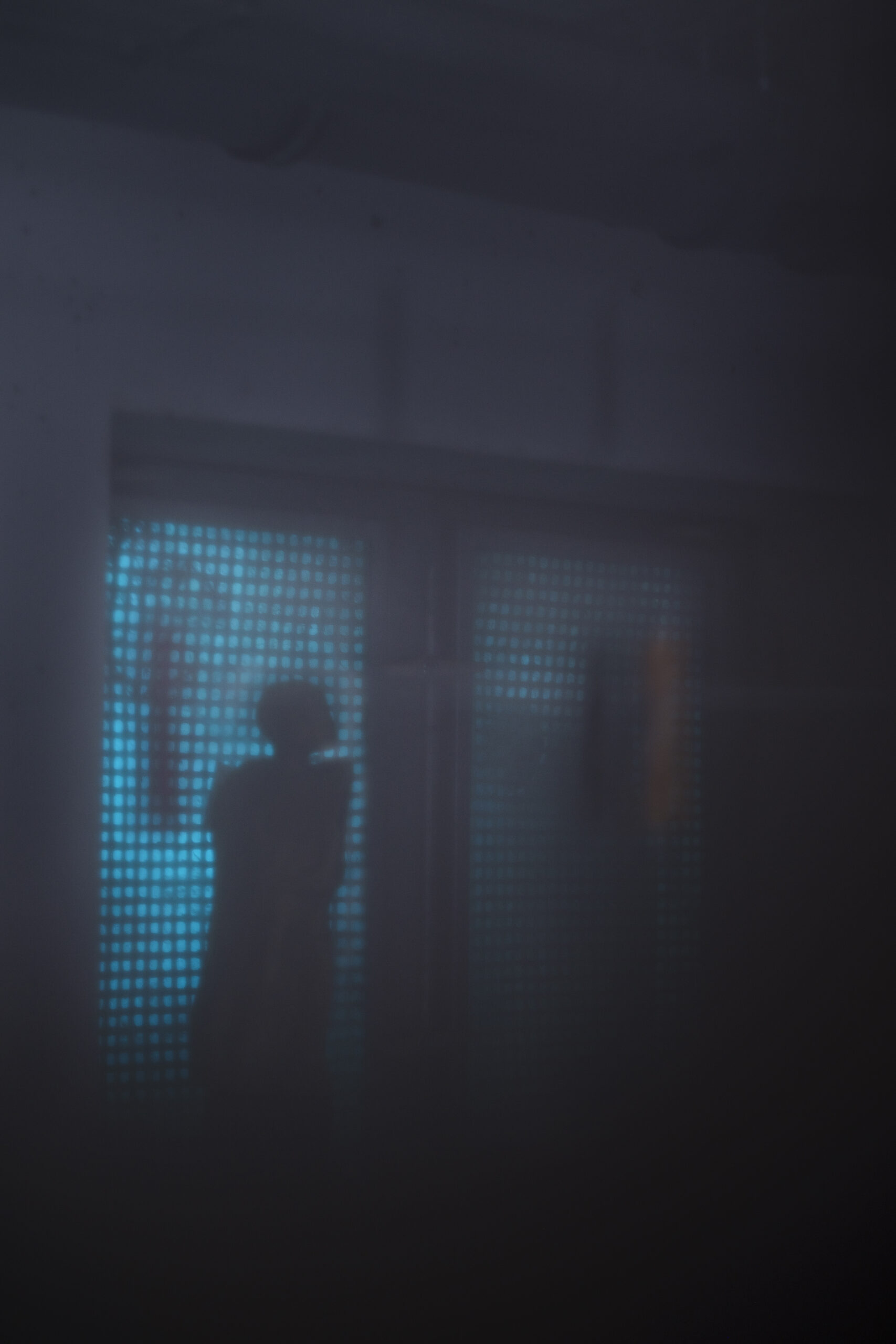 Schemenhafter Umriss einer Tonfigur vor einem Kellerfenster, von außen dringt unheimliches blaues Licht ein, dunkle, gespenstische Stimmung