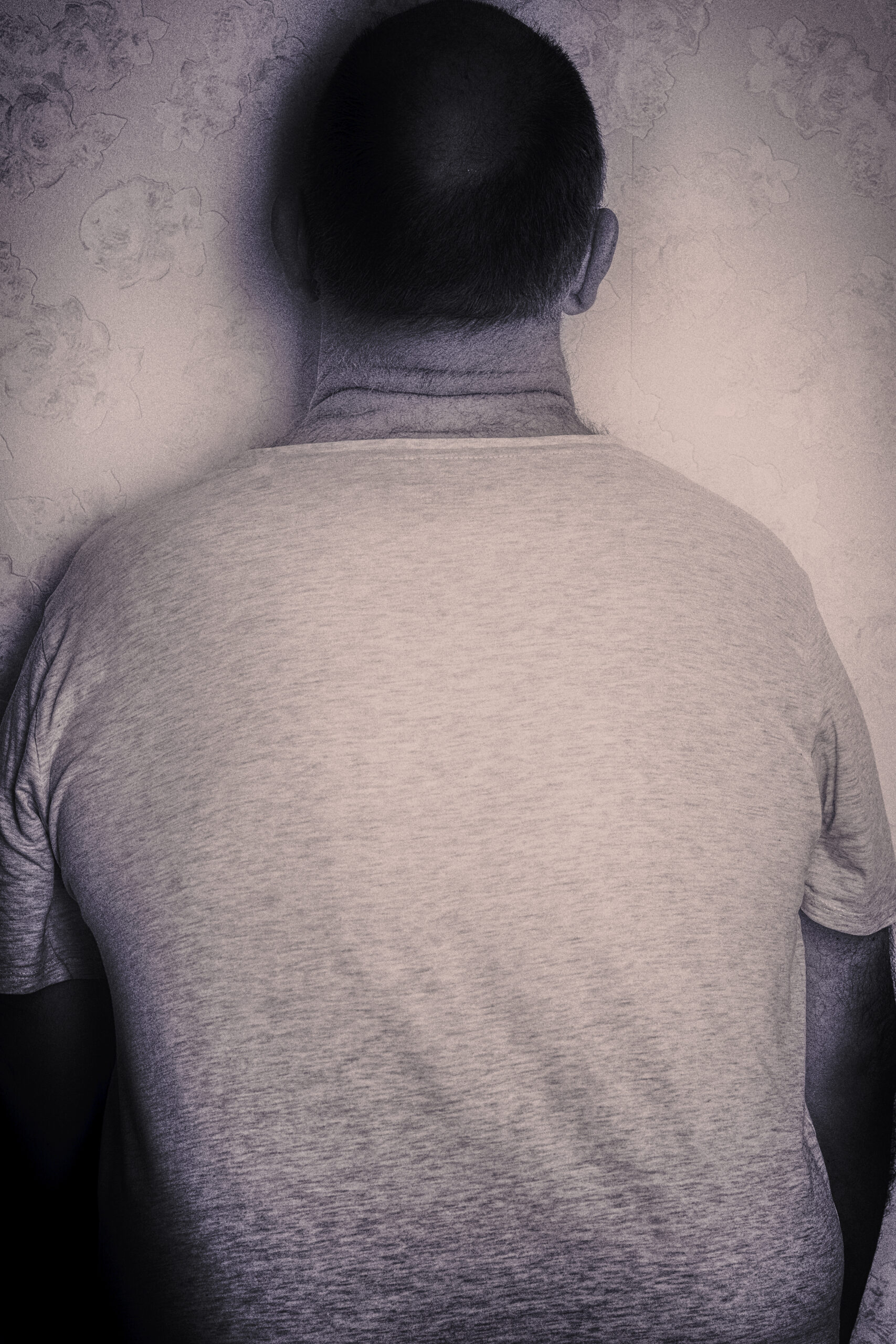 Mann steht mit dem Gesicht zur Wand, Halbportrait, entsättigte Farben, sepia-tönung