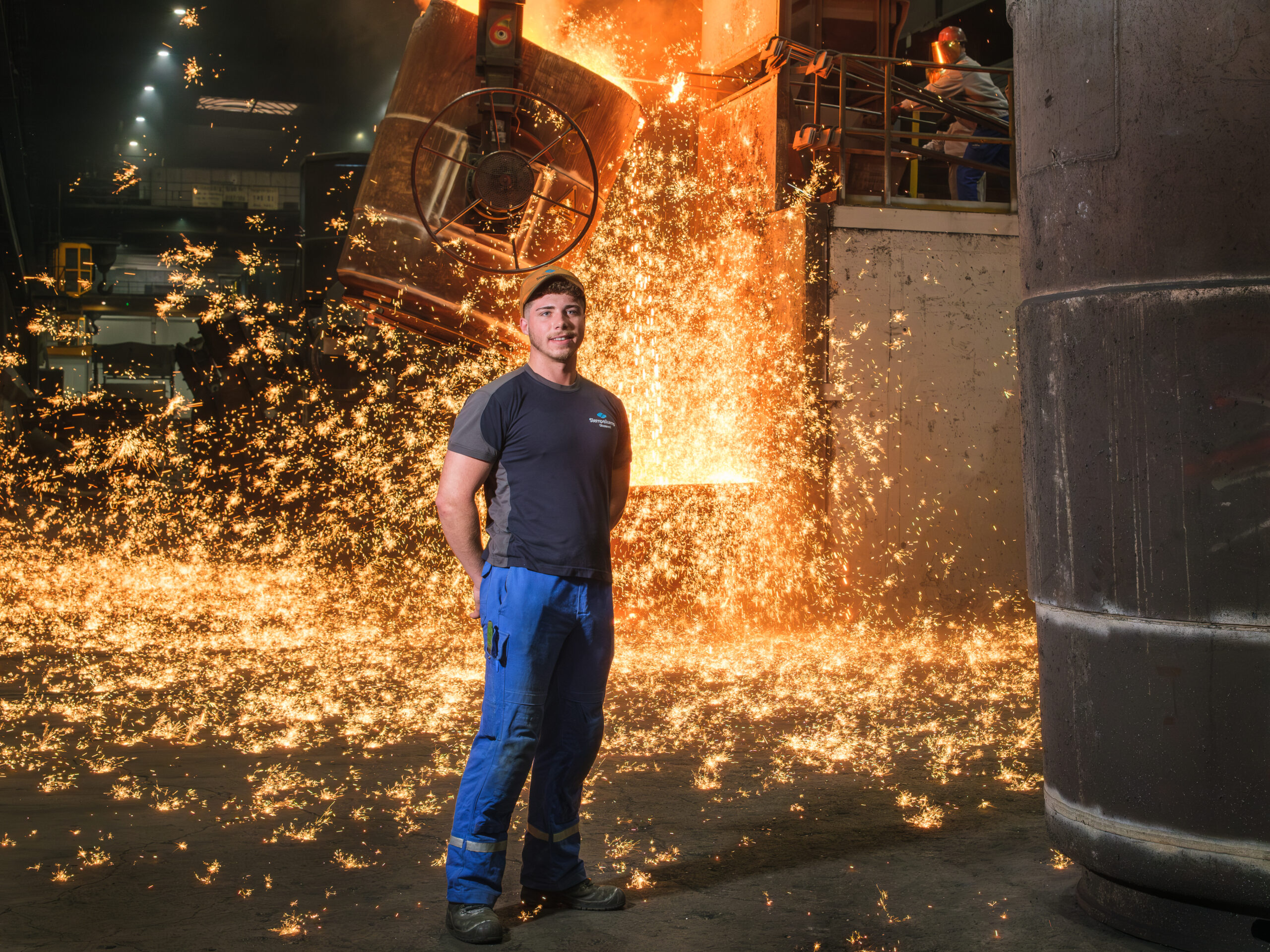 Azubi-Projekt-Firma Siempelkamp-2 Auszubildender in der Metallindustrie steht in der Gießerei vor funkanschlagendem Hochofen