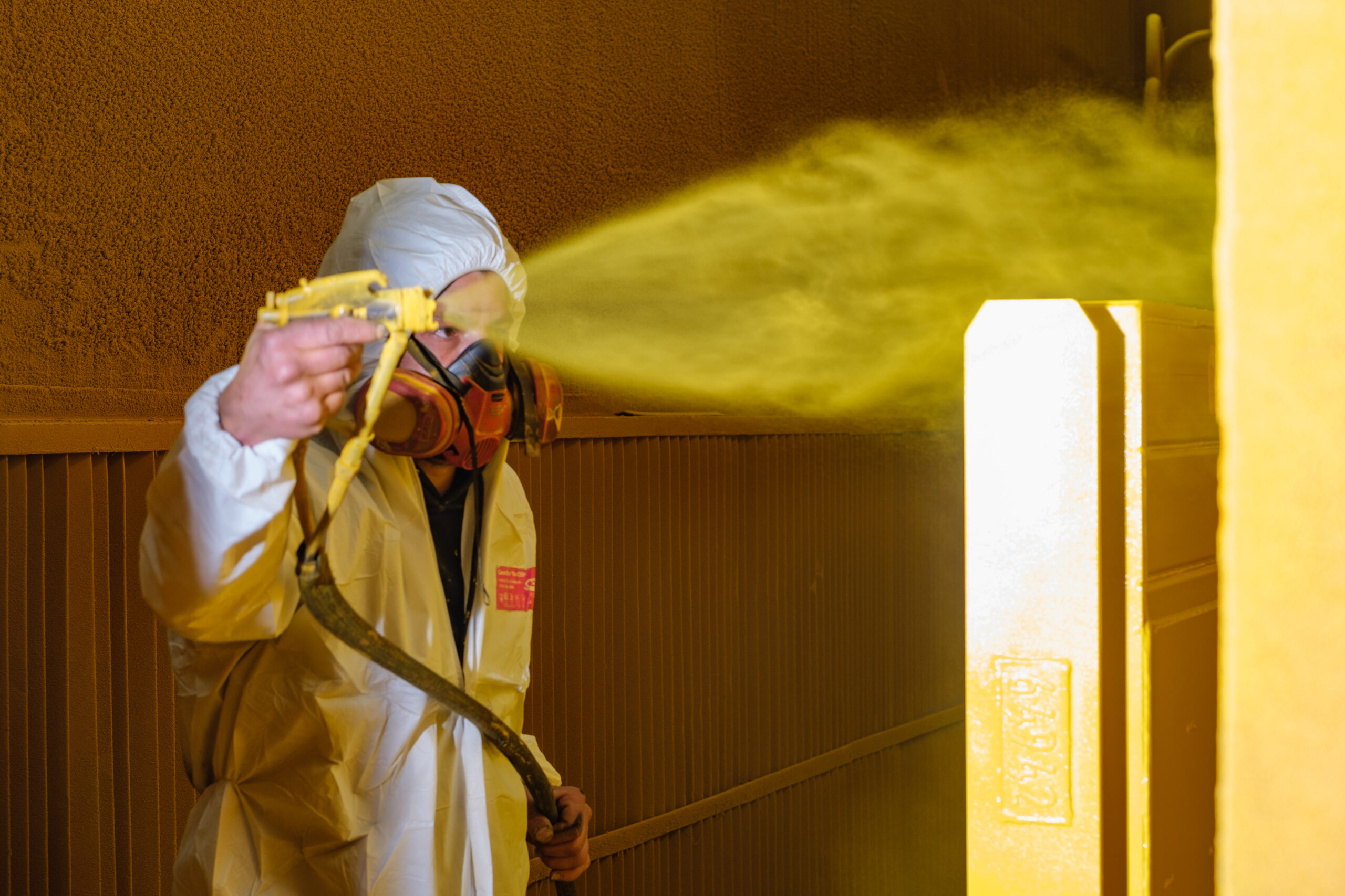Lackierarbeiten Firma TWF Heinsberg Lackierer sprüht in einer Lackierstraße einen großen Metallgegenstand gelb an