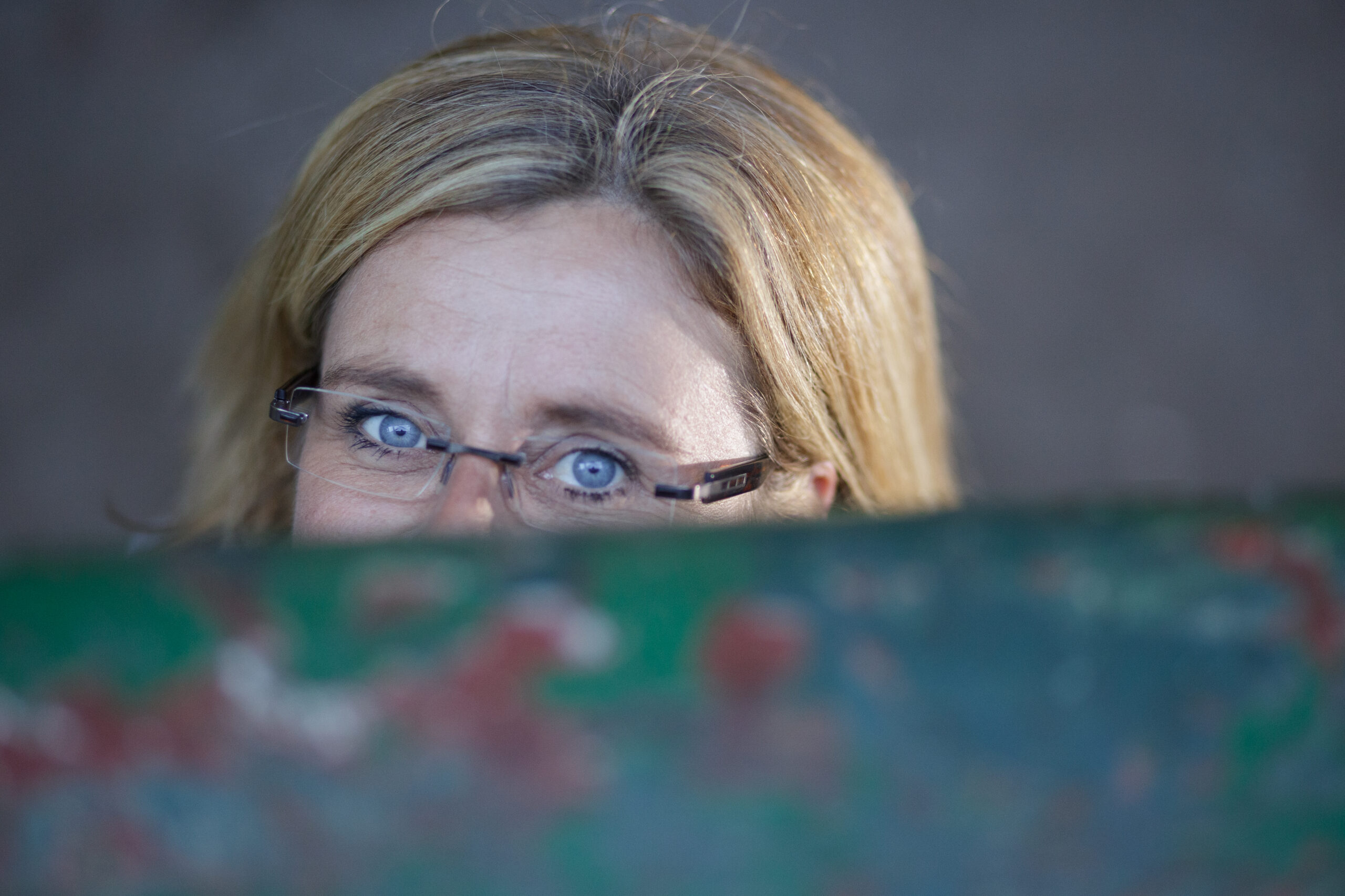 Schau mich an! Frau mit strahlend blauen Augen schaut über einen Metallgegenstand, Nase und Mund verdeckt
